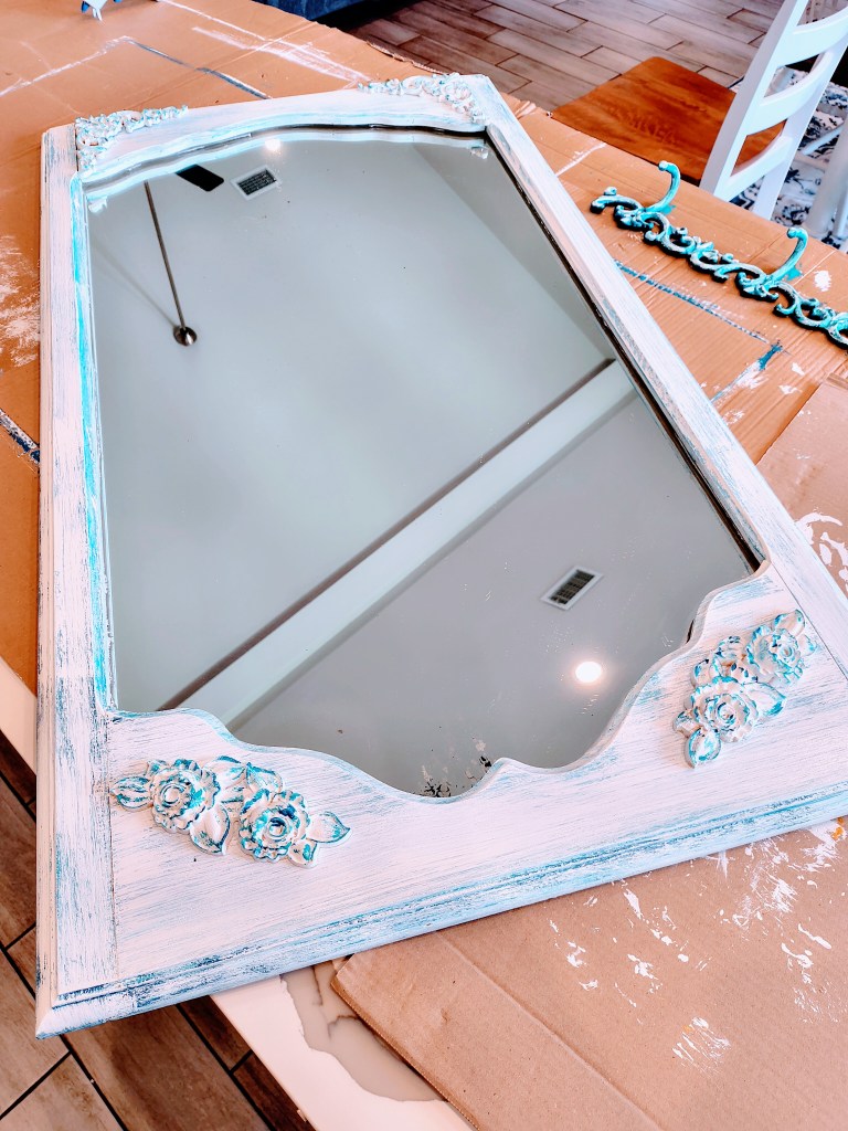 Vintage mirror makeover, after photo.  Painted in blue and white with wooden appliques.
acrossthelake.blog