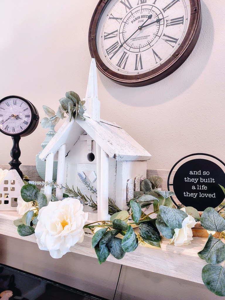 Vintage white church birdhouse with fresh paint and faux florals displayed as home decor.
acrossthelake.blog