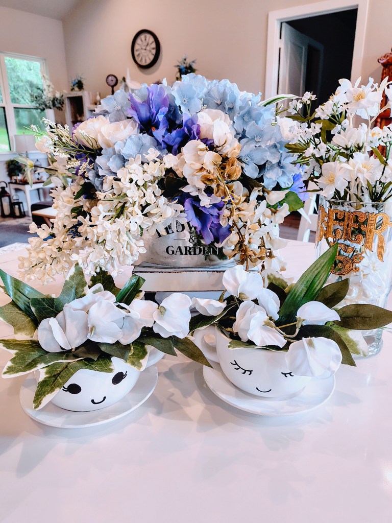 Faux floral arrangements in various misc. vases/holders in blues and whites.
acrossthelake.blog