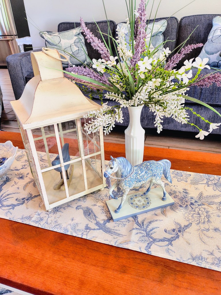 Purple and white faux floral arrangement in a white milk glass vase.
acrossthelake.blog