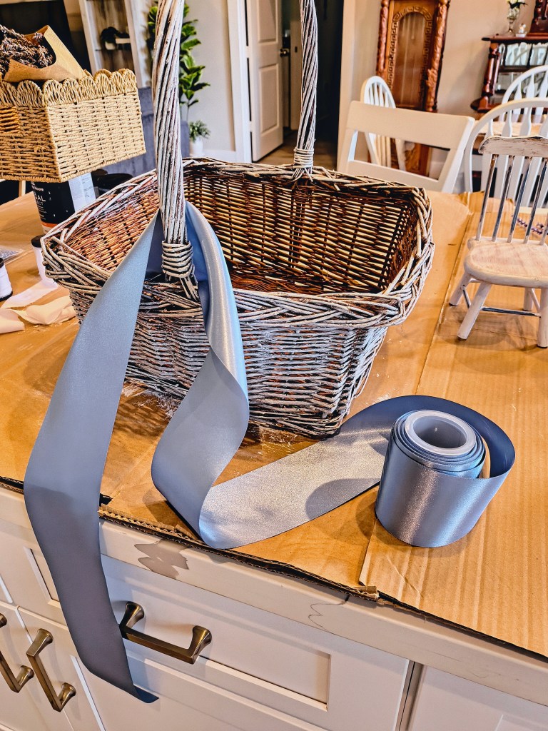 Wicker basket painted white with dusty blue satin ribbon to be tied.
acrossthelake.blog